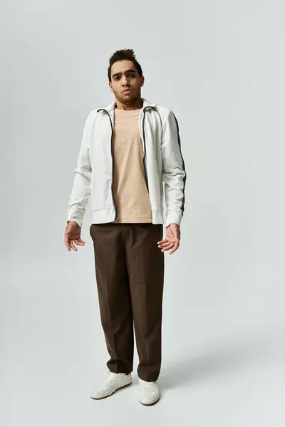 A young African American man in a white jacket, brown pants, and white sneakers poses against a grey background. — Stock Photo