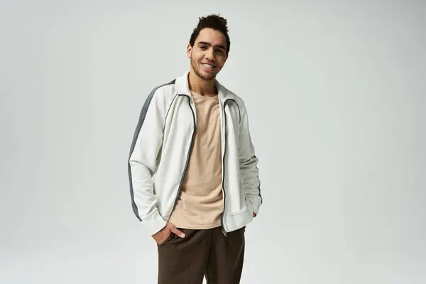 A young African American man in a stylish white jacket poses against a grey background. — Stock Photo