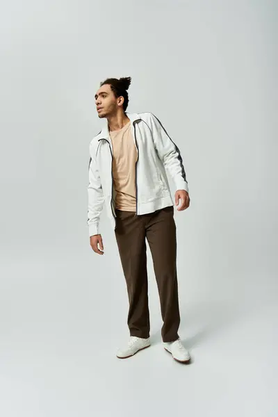 A young African American man poses in a stylish white jacket and brown pants against a gray background. — Stock Photo