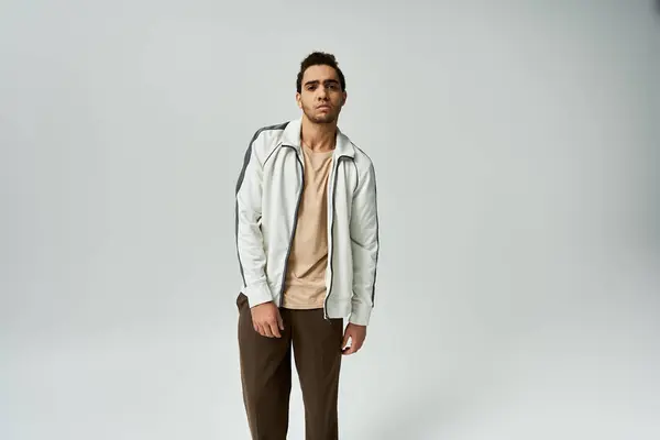 A young African American man is wearing a white jacket and posing against a grey backdrop. — Stock Photo