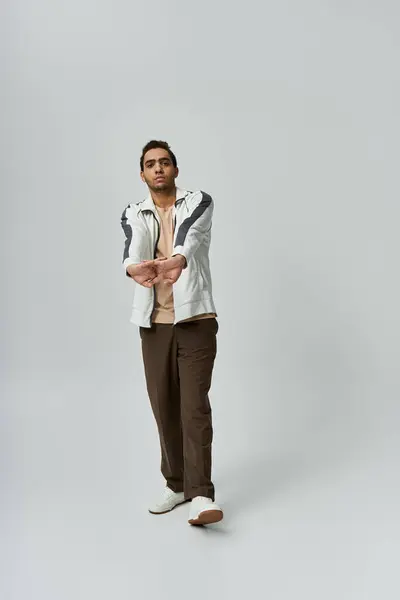 A young African American man in a white jacket and brown pants poses against a grey background. — Stock Photo