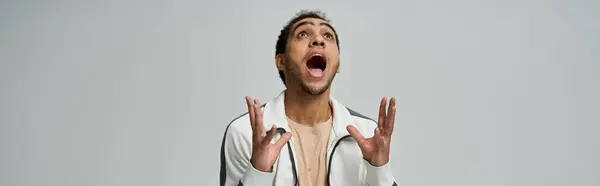 A young African American man in a stylish outfit poses against a grey background, his mouth open in a wide, excited expression. — Stock Photo