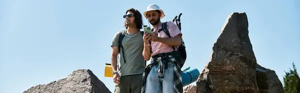 Dois jovens, um casal gay, caminham juntos através de uma paisagem selvagem rochosa em um dia ensolarado de verão. — Fotografia de Stock