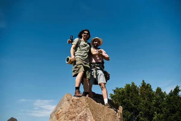 A young gay couple smiles and looks at the camera while hiking in the wilderness on a sunny summer day. — Stock Photo