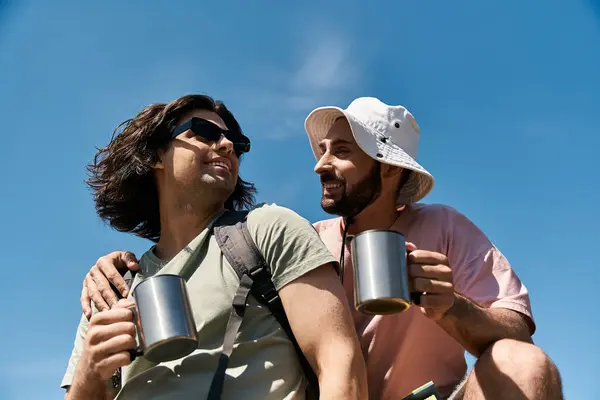 Two young gay men are hiking in nature, enjoying coffee on a sunny summer day. — Stock Photo