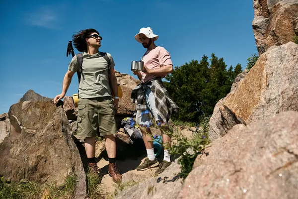 Two young men, a gay couple, hike through a rocky wilderness on a sunny summer day. — Stock Photo