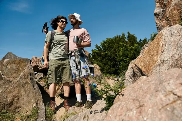 Two young men, a gay couple, hike together in a rocky wilderness setting during a sunny summer day. — Stock Photo