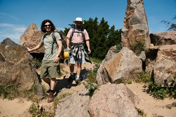 Um jovem casal gay caminhadas deserto rochoso em roupas casuais e mochilas, desfrutando de vistas panorâmicas em um dia ensolarado de verão. — Fotografia de Stock