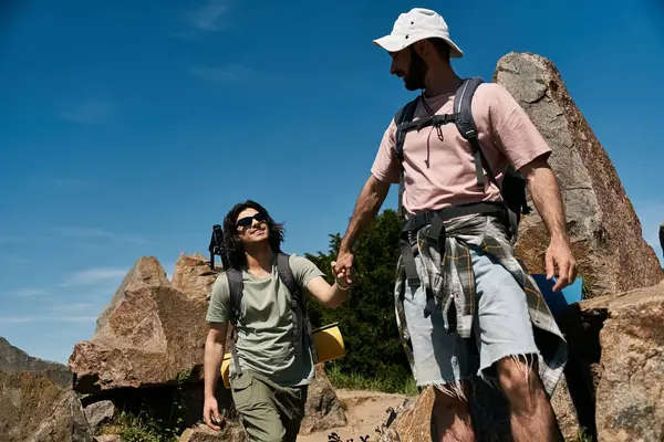 Um jovem casal gay caminha através de uma paisagem rochosa, apreciando a luz do sol de verão e companhia uns dos outros. — Fotografia de Stock