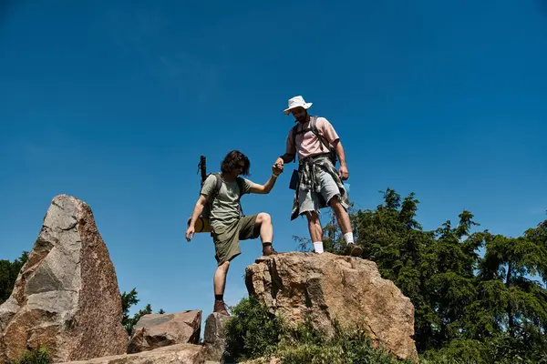 Dois jovens caminham juntos num dia ensolarado. Eles estão ajudando uns aos outros em uma trilha rochosa no deserto. — Fotografia de Stock