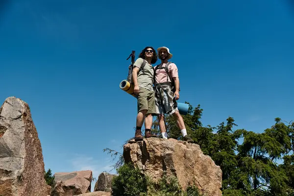 Due giovani, una coppia gay, passeggiano insieme nella natura in una giornata estiva. Si trovano su un affioramento roccioso, godendo della vista. — Foto stock
