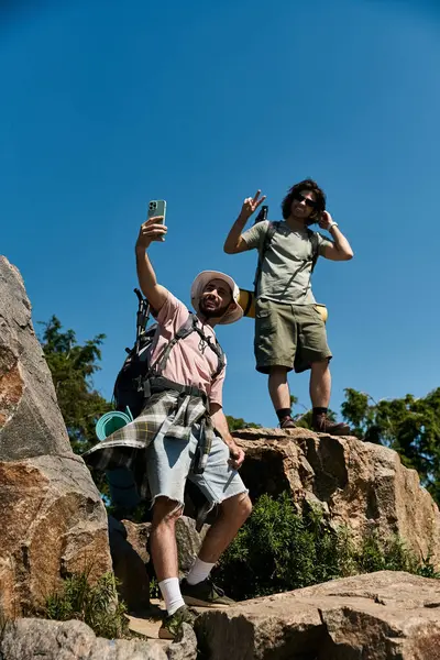 Two young men hike together in the wilderness, taking a selfie on a rocky mountaintop. — Stock Photo
