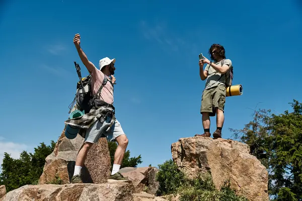 A young gay couple celebrates reaching a mountain peak during a summer hike. — Stock Photo