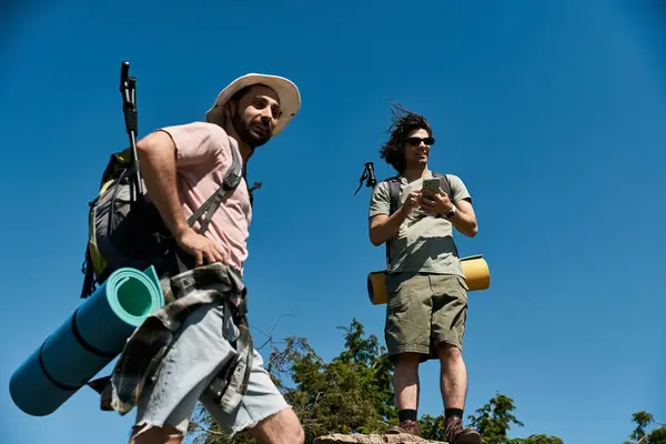 Dois jovens, um casal gay, caminham juntos na natureza em um dia ensolarado de verão. Eles estão desfrutando do ar livre e da vista de um ponto alto. — Fotografia de Stock