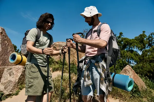Dois jovens caminham por uma paisagem de verão, usando postes de trekking para navegar pelo terreno. — Fotografia de Stock