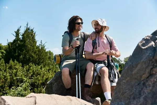Um casal gay gosta de uma caminhada de verão, fazendo uma pausa para admirar a vista de um afloramento rochoso. — Fotografia de Stock