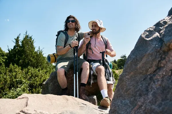 A gay couple enjoys a summer hike, resting on a rocky outcrop in the wilderness. — стоковое фото