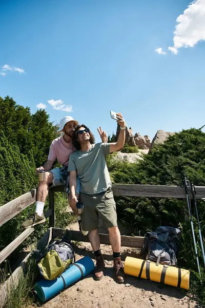 A gay couple enjoys a summer hike, taking a selfie with a view of the wilderness behind them. — Stock Photo