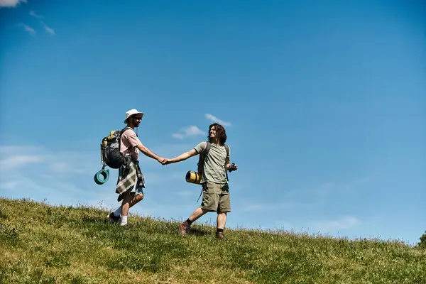 A young gay couple walks hand-in-hand on a grassy hilltop on a sunny summer day. — Stock Photo