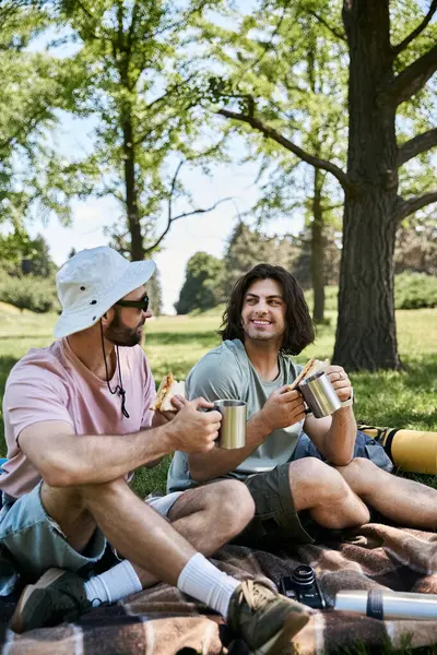 Um jovem casal gay desfruta de um piquenique em uma caminhada de verão, fazendo uma pausa para relaxar e compartilhar uma refeição. — Fotografia de Stock