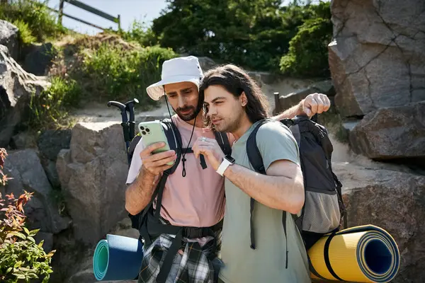 Two young men, a gay couple, hike through nature on a sunny day, checking their phone for directions. — Stock Photo