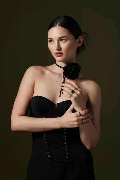 Una giovane donna con i capelli castani posa in un corsetto nero, indossando una collana di girocollo fiore. — Foto stock