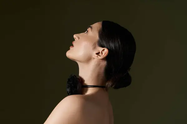 A young woman with dark hair poses against a black background, wearing a flower choker necklace. — Stock Photo
