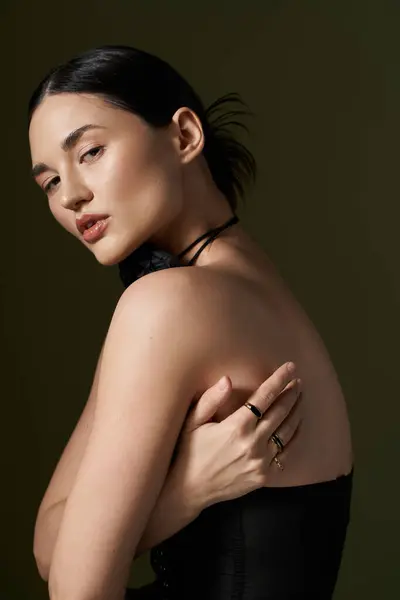 A young, beautiful woman with brunette hair poses against a black background, wearing a flower choker necklace and a black dress. — Stock Photo