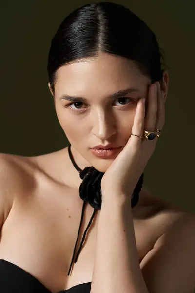 Uma jovem mulher com cabelo escuro e uma gargantilha de flores olha atentamente para a câmera, sua mão descansando suavemente em sua bochecha. — Fotografia de Stock