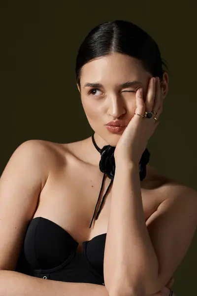 A young woman with brunette hair poses for the camera while wearing a flower choker and a black top against a dark background. — Stock Photo