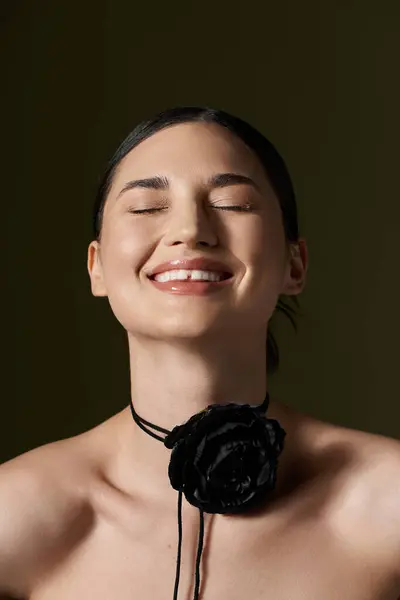 A young woman with brunette hair smiles brightly, adorned with a black flower choker necklace against a dark background. — Stock Photo