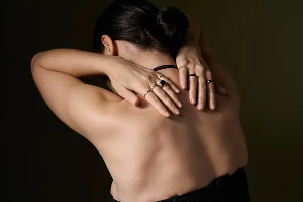 A young woman with long, dark hair poses against a black background, showcasing her back and delicate jewelry. — Stock Photo
