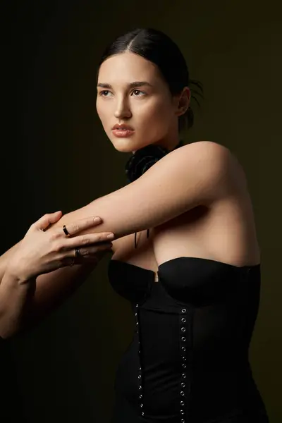 A young woman with dark hair poses against a black backdrop, wearing a black corset and a flower choker necklace. — Stock Photo