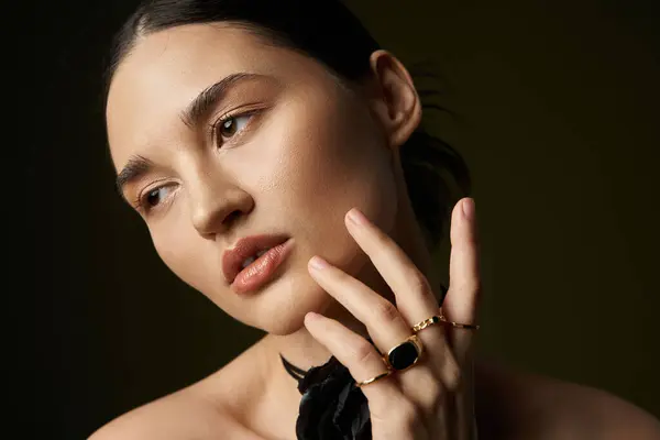 A young woman with long brunette hair poses against a black background. She is wearing a flower choker and several rings. — Stock Photo