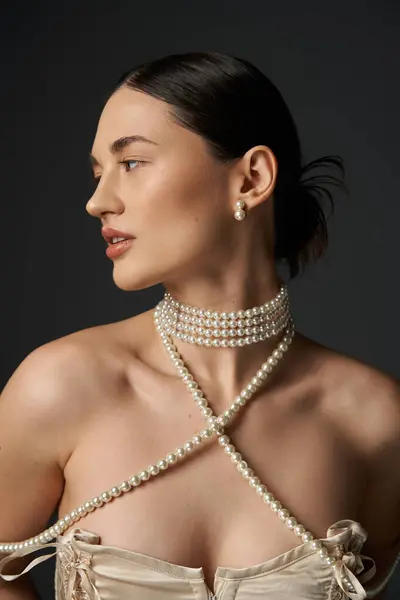 A young woman with brunette hair and a pearl necklace poses against a dark background. — Stock Photo