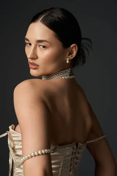 Uma jovem mulher com cabelo morena e um colar de pérolas posa contra um fundo escuro, mostrando seu estilo elegante e beleza atemporal. — Stock Photo