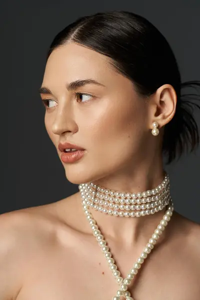 A young woman with brunette hair wears a pearl necklace and earrings against a dark backdrop. — Stock Photo