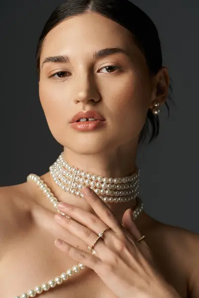 A young woman with brunette hair poses in a pearl necklace and earrings against a dark background. — Stock Photo