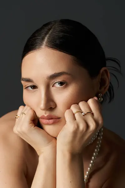 Eine junge Frau mit brünetten Haaren posiert, ihr Kinn auf den Händen liegend, mit zartem Schmuck verziert. — Stockfoto