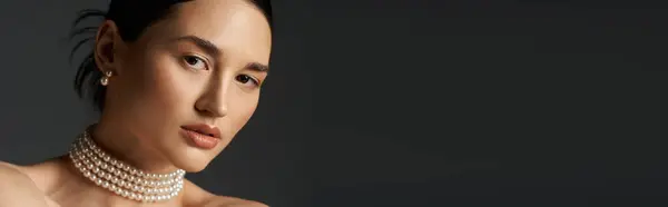Una bella donna dai capelli scuri, con indosso una collana di perle, guarda direttamente lo spettatore sullo sfondo scuro. — Foto stock