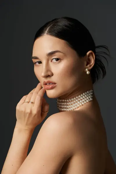 A young woman with long brunette hair and a pearl necklace poses against a dark backdrop. — Stock Photo