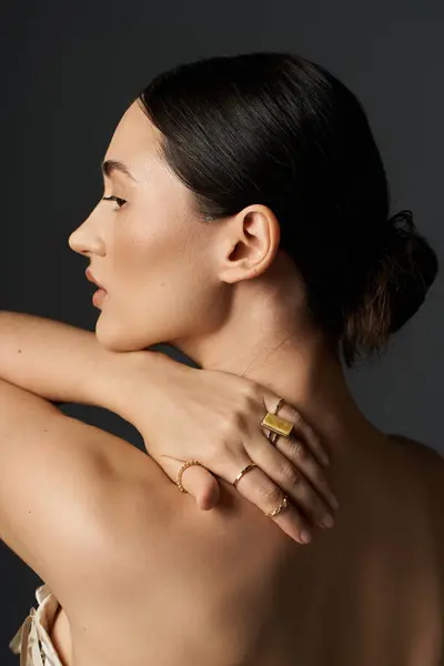 A young woman with dark hair poses against a dark background, showcasing her gold rings on her fingers. — Stock Photo