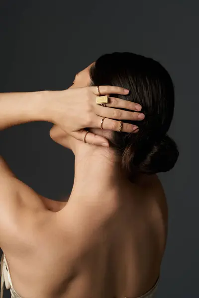 Una joven con el pelo moreno se muestra desde la espalda, mostrando sus anillos dorados en sus dedos sobre un fondo oscuro. — Stock Photo