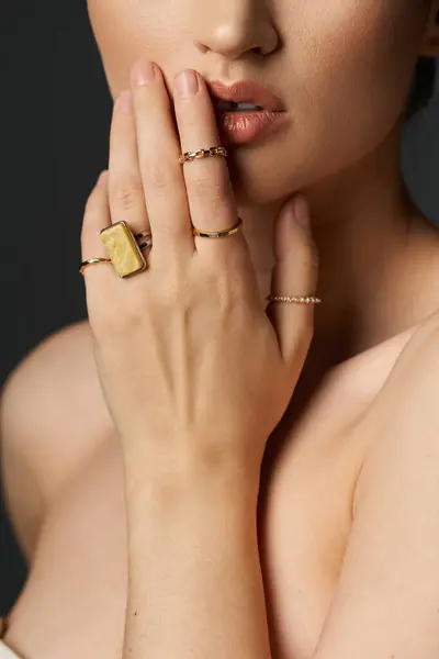 Una giovane donna con i capelli scuri mostra i suoi anelli d'oro sulle dita su uno sfondo scuro. — Foto stock