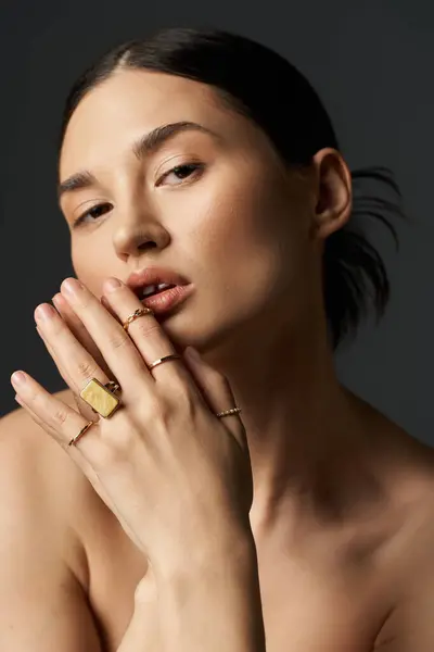 A young woman with dark hair and flawless skin poses against a dark background, showcasing her golden rings. — Stock Photo