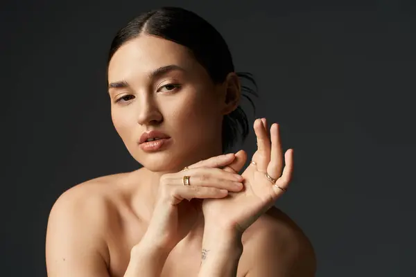 A woman with dark hair poses against a dark background, her fingers adorned with gold rings, looking thoughtful. — Stock Photo