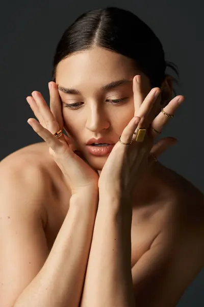 A young woman with dark hair poses against a dark background, showcasing her golden rings on her fingers. — Stock Photo