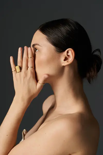 A young woman with dark hair poses against a dark background, showcasing her golden rings. — Stock Photo
