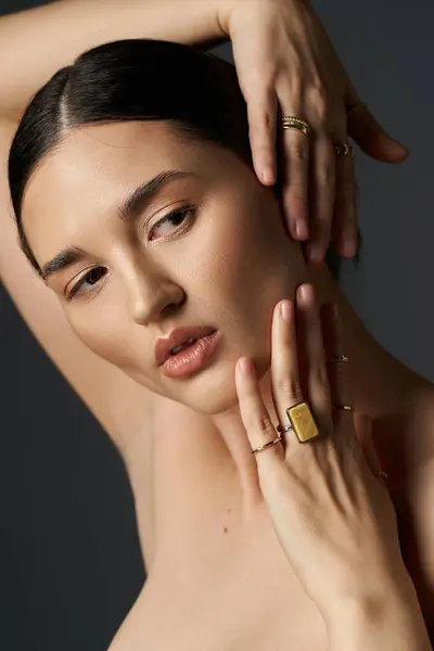 Eine junge Frau mit dunklen Haaren trägt goldene Ringe vor dunklem Hintergrund und legt ihre Hand zart auf die Wange. — Stockfoto