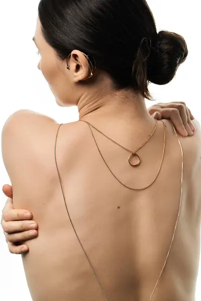A young woman with dark hair highlights gold necklaces and ear cuffs against a white background, creating a stunning portrait from behind. — Stock Photo